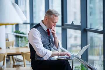 Adult male businessman, teacher, mentor working on a new project. Sits by a large window on the...