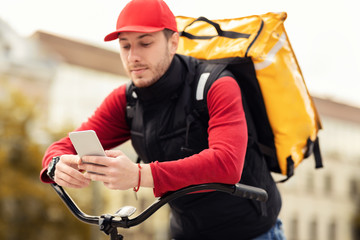 Fototapeta premium Courier Using Delivery Application On Phone Sitting On Bicycle Outside
