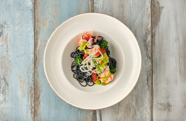 Black Italian seafood pasta with shrimps, cherry tomatoes and greens. Pasta with cuttlefish ink, cooked sea food macaroni.