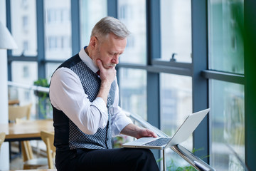 Adult male businessman, teacher, mentor working on a new project. Sits by a large window on the...