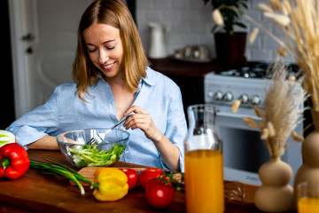 Young woman in kitchen having dinner - healthy green salad in bowl