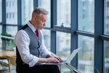 Adult male businessman, teacher, mentor working on a new project. Sits by a large window on the...