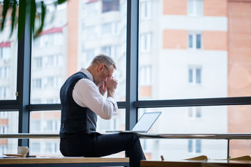 Adult male businessman, teacher, mentor working on a new project. Sits by a large window on the...