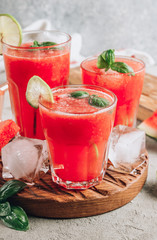 Watermelon lemonade with lime and fresh basil leaves on concrete background. Refreshing summer drink