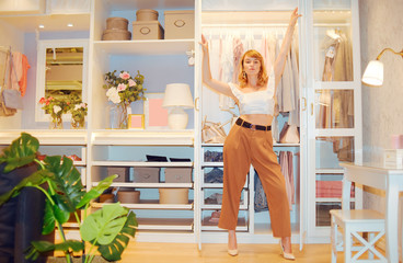 Girl model posing against the backdrop of a wardrobe with clothes. Woman in trousers and white top showing her room  gardirop