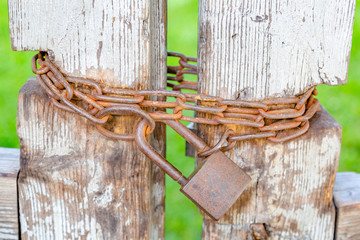 Old crooked gate closed on a large rusty padlock with chains