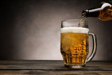 pouring blonde beer into glass pint on wooden table