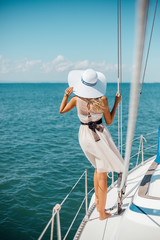 Romantic girl in a hat and dress floats on a white yacht on the sea. Vertical orientation.