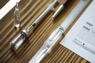 Fototapeta premium A man signs a medical document. Medical equipment on the table. Stethoscope and ampoules with syringes. Makes notes in the office. Medical center.