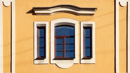 brown old three windows in white frame and pediment on yellow wall