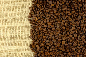 Fototapeta premium Coffee bean heap on sack background closeup. Coffee pile on rush mat with macro.
