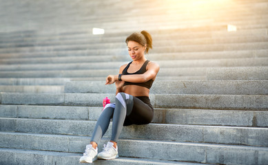 Athletic black woman sitting on stairs, checking on smartwatch