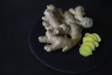 Ginger root whole and sliced. Ginger tea with lemon on the dark background. Fresh ginger root on stone background. Vitamins. Free space for your text.