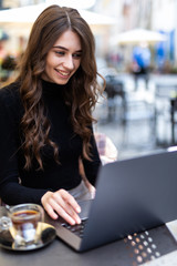 Beautiful young woman using laptop at outdoors cafe