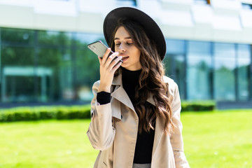 Beauty female student talking with smartphone hands free system while holding a folder on campus of...