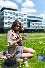 Fototapeta na wymiar Beautiful young student girl sitting on green grass, on the lawn and working behind a black laptop with a mobile phone