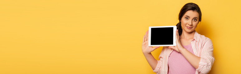 panoramic shot of pregnant woman showing digital tablet with blank screen on yellow