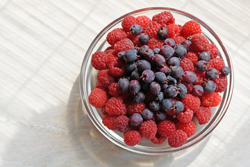 On the white tabletop is a glass plate with red raspberries and blue Irga berries
