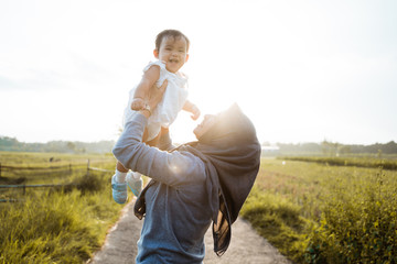 Fototapeta premium Asian mother raising her daughter when standing the road in the middle of the rice fields on a sunny summer day