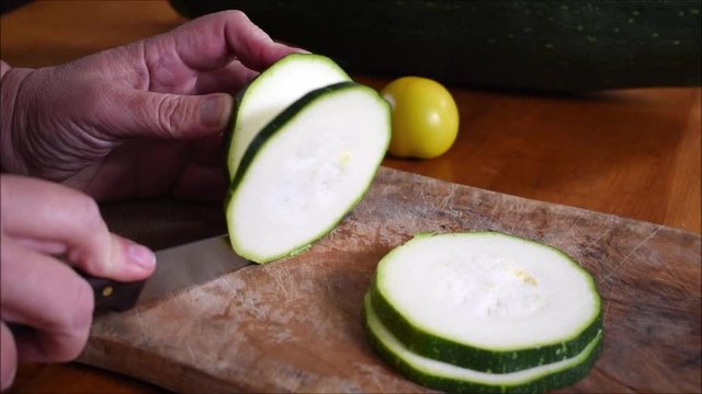 Schneiden von Zucchini, Zucchinist&uuml;cke von gro&szlig;em Zucchinischneiden, Gem&uuml;se schneiden auf Holzbrett, aus dem Garten auf den Tisch