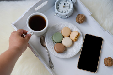 white wooden tray with black tea, coffee, plate with macaroon cakes, alarm clock, blank screen...