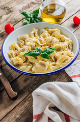 Tortellini with cheese sauce, basil leaves in bowl on rustic wooden table.