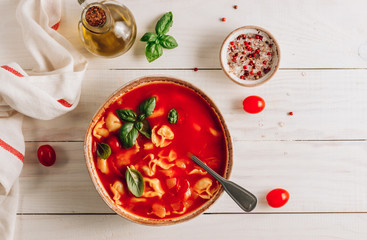 Tomato soup with tortellini in white bowl on white wooden table.