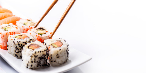 Closeup of sushi roll dish with bamboo chopstick frame isolated on white background. Luxury japanese restaurant dinner with sashimi, maki, surimi and soy sauce on plate.