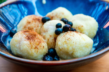 Six homemade sweet dumplings served with vanilla cream and blueberries in blue ceramic vintage bowl