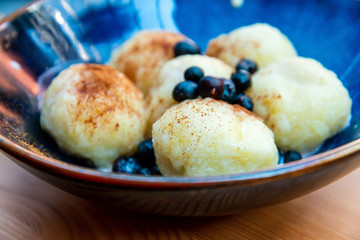 Six homemade sweet dumplings served with vanilla cream and blueberries in blue ceramic vintage bowl