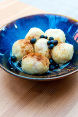 Six homemade sweet dumplings served with vanilla cream and blueberries in blue ceramic vintage bowl