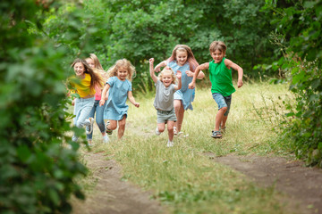 Obraz premium Happiness. Kids, children running on green forest. Cheerful and happy boys and girs playing, laughting, running through green blooming meadow. Childhood and summertime, sincere emotions concept.