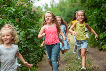 Fototapeta premium Happiness. Kids, children running on green forest. Cheerful and happy boys and girs playing, laughting, running through green blooming meadow. Childhood and summertime, sincere emotions concept.