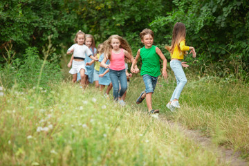 Obraz premium Carefree. Kids, children running on green forest. Cheerful and happy boys and girs playing, laughting, running through green blooming meadow. Childhood and summertime, sincere emotions concept.