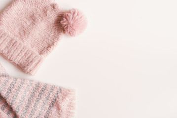 Handmade knitted hat and scarf of pink color on white background, top view, copy space. Warm clothing concept