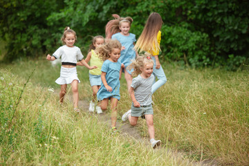 Fototapeta premium Carefree. Kids, children running on green forest. Cheerful and happy boys and girs playing, laughting, running through green blooming meadow. Childhood and summertime, sincere emotions concept.