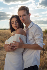 portrait of a young guy and a girl twenty two years old. Generation Z wedding. Against the backdrop of a cloudy sky, a setting sun in a field