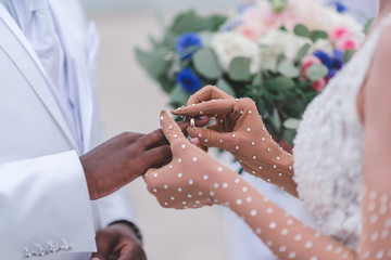Emotionally touching happy moment of swapping wedding rings during beach ceremony, caucasian bride and african groom. Northsea, Germany.