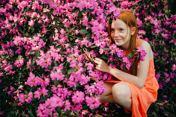 Obraz na płótnie Canvas Picture of an amazing red-haired baby girl in an orange dress enjoying a pastime in the big spring garden
