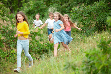 Obraz premium Best time. Kids, children running on green forest. Cheerful and happy boys and girs playing, laughting, running through green blooming meadow. Childhood and summertime, sincere emotions concept.