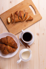a white ceramic cup of black roasted coffee espresso and a french croissant on the wooden surface