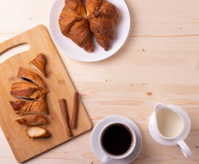 a white ceramic cup of black roasted coffee espresso and a french croissant on the wooden surface