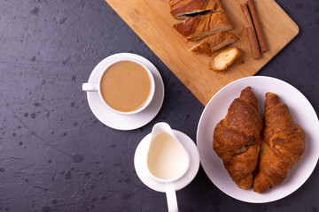 a white ceramic cup of black roasted coffee espresso and a french croissant on the wooden surface