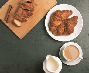a white ceramic cup of black roasted coffee espresso and a french croissant on the wooden surface
