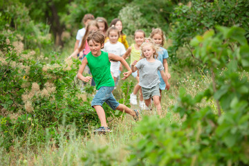 Best time. Kids, children running on green forest. Cheerful and happy boys and girs playing, laughting, running through green blooming meadow. Childhood and summertime, sincere emotions concept.