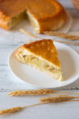 A piece of round pie and wheat stalks on white background