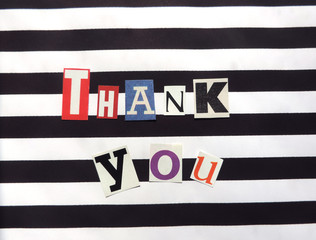 thank you words made from paper letters cut from magazines on a striped black and white surface .  