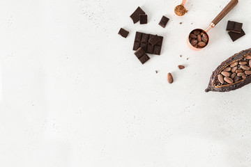 Dark chocolate pieces crushed, cocoa powder and cocoa beans in pod on white concrete background. Culinary food background, top view, copy space. Natural chocolate
