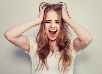 Obraz premium Angry young blong woman strong screaming with wide open mouth on light blue background. Closeup portrait