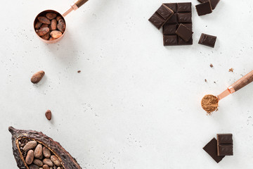 Flat lay composition with cocoa beans, chocolate pieces, cocoa powder and pods on white concrete background. Organic food, natural chocolate. Top view, copy space.